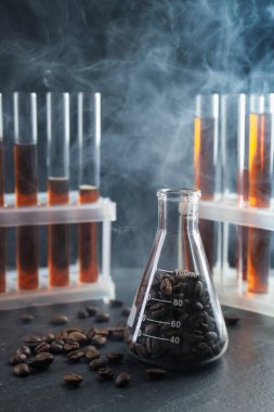 Kahve, fasulye ve dumanlı laboratuvar bardakları siyah masada, yakın plan.