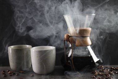 Cam kimya kahve makinesi, lezzetli kahve, fasulye ve fincanlar gri masada, yakın plan.