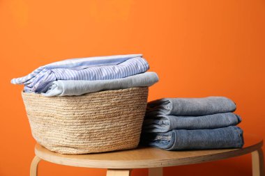 İçerideki turuncu duvarın yanındaki ahşap masada giysileri olan çamaşır sepeti.