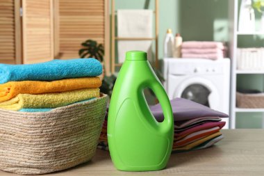 Çamaşır sepetinde havlular, giysiler ve kapalı masa üzerinde bir şişe deterjan.