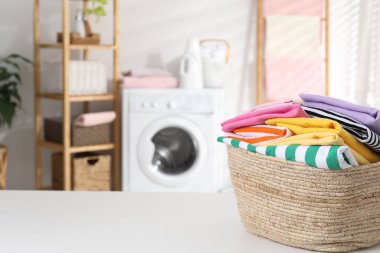 Çamaşır sepetinin içinde beyaz masa üzerinde giysiler var. Metin için boşluk