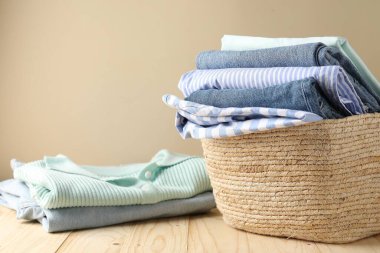 İçerideki bej duvarın yanındaki ahşap masada giysileri olan çamaşır sepeti, yakın plan. Metin için boşluk