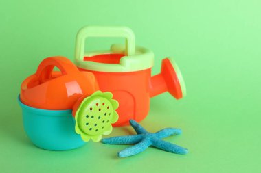 Plastik sulama kutuları ve yeşil arka planda deniz yıldızı, metin için yer. Çocuklar için plaj oyuncakları