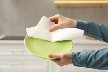 Kadın mutfakta kağıt havluyla tabağı siliyor, yakın plan.