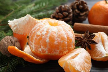 Olgun mandalinalar, baharatlar, ceviz, köknar ağacı dalları ve tahta masanın üzerindeki koniler, yakın plan.