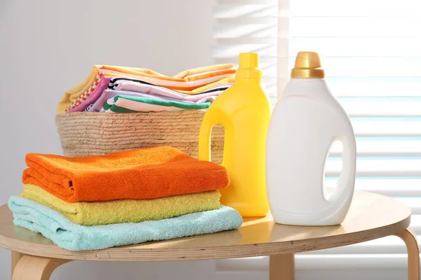 Çamaşır sepetinin içinde giysiler, havlular ve kapalı masa üzerindeki deterjan şişeleri.