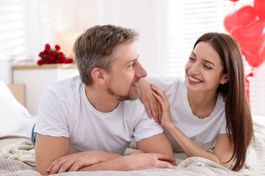 Yataktaki mutlu çift kalp şeklinde balonlarla süslenmiş. Sevgililer Günü kutlaması