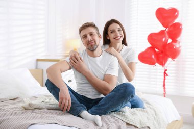 Yataktaki mutlu çift kalp şeklinde balonlarla süslenmiş. Sevgililer Günü kutlaması