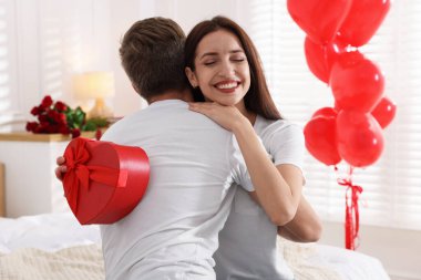 Sevgililer günü hediyesi olan mutlu bir kadın erkek arkadaşına evde sarılıyor.