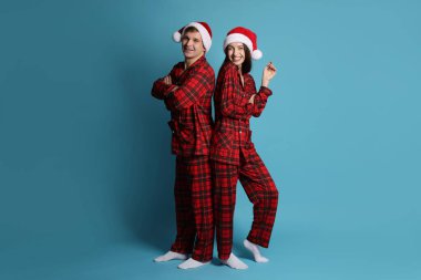 Açık mavi arka planda Noel Baba şapkalı ve pijamalı mutlu bir çift. Noel atmosferi