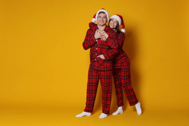 Turuncu arka planda Noel Baba şapkalı ve pijamalı mutlu çift, mesaj için yer var. Noel atmosferi