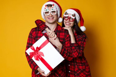 Noel Baba şapkalı ve pijamalı mutlu çift. Noel hediyeleri turuncu arka planda. Mesaj atmak için yer var.