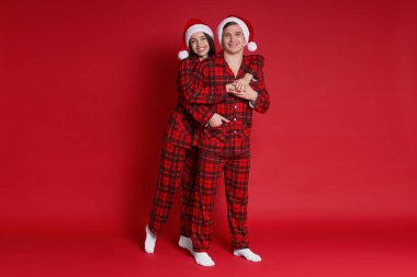 Kırmızı arka planda Noel Baba şapkalı ve pijamalı mutlu çift. Noel atmosferi