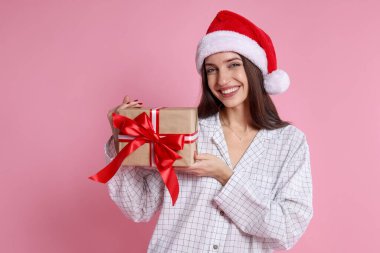 Noel Baba şapkalı mutlu kadın pembe arka planda Noel hediyesi, mesaj için yer var.