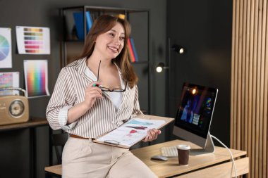 Ofiste gözlüklü ve kıyafet çizimi yapan tasarımcı.