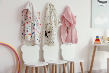 Oyun odasındaki ışıklı duvarda şık sandalyeler ve elbiseler asılı.