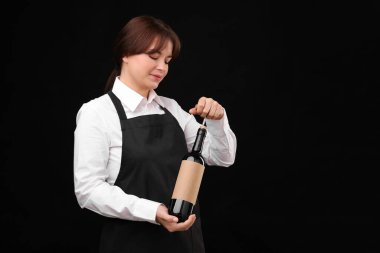 Profesyonel şarap garsonu. Siyah arka planda şarap şişesi açıyor. Mesaj için yer var.