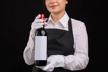 Siyah arka planda kırmızı şarap şişesi olan profesyonel şarap garsonu.