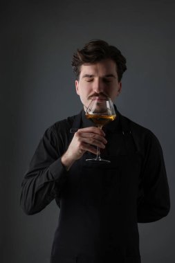 Profesyonel şarap garsonu gri arka planda beyaz şarap tadıyor.