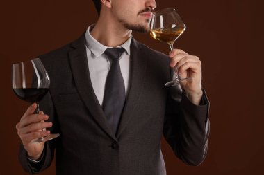 Profesyonel şarap garsonu kahverengi arka planda şarap tadıyor.