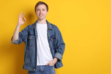 Yakışıklı genç adam sarı arka planda iyi niyet göstergesi gösteriyor. Metin için boşluk