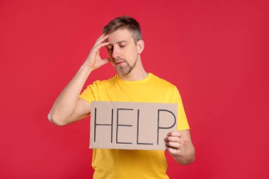 Mutsuz adam kırmızı arka planda kelime yazılı karton tabela tutuyor.
