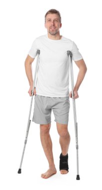 Beyaz arka planda yaralı bacağı ve koltuk değneği olan bir adam.