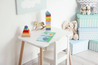 Oyun odasındaki beyaz masada farklı oyuncaklar ve kitap. İç tasarım