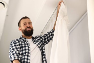 Evde pencere perdelerini asan adam, düşük açılı görüntü.