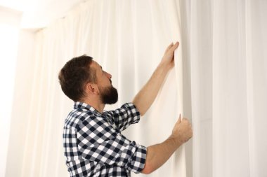 Evde pencere perdelerini asan adam, düşük açılı görüntü.