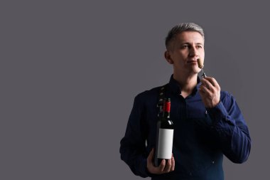 Gri arka planda kırmızı şarap şişesi ve tirbuşonu olan profesyonel şarap garsonu.