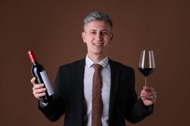 Kahverengi arka planda kırmızı şarap ve şişe kadehi olan profesyonel şarap garsonu.