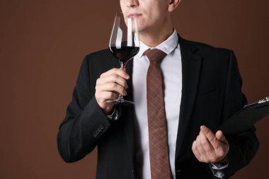 Profesyonel şarap garsonu. Kahverengi arka planda kırmızı şarap tadıyor. Mesaj için yer var.
