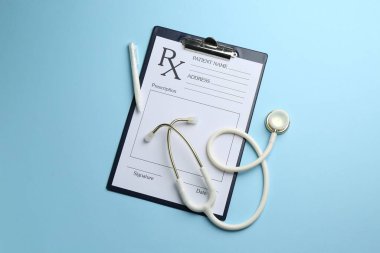 Boş alanlar, steteskop ve açık mavi arka planda kalem içeren tıbbi reçete formu, düz uzanma