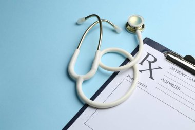 Açık mavi arkaplanda steteskop ve boş tarlalarla tıbbi reçete formu, yakın plan. Metin için boşluk