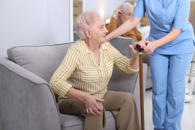Bakım işçisi yaşlı kadına bastonuyla yardım ediyor huzurevinde koltuktan kalkması için, yakın plan.
