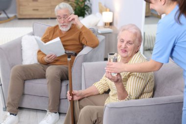 Huzurevindeki yaşlı kadına bir bardak su veren bakım görevlisi, yakın plan.