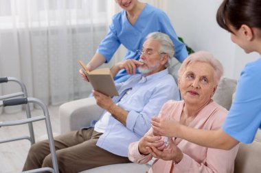 Bakım işçileri huzurevindeki yaşlı adam ve kadına yardım ediyor. Kapatıyorlar.