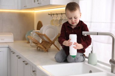 Evde çocuk güvenliği. Küçük çocuk mutfakta lavabonun yanında tozla oynuyor, mesaj için yer var.