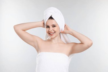 Açık gri arka planda, havluya sarılı saçları olan bir kadın.