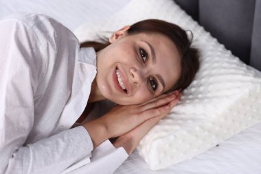 Ortopedik yastıkla yatakta yatan gülümseyen kadın. Sağlıklı duruş