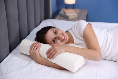 Evde ortopedik yastıkla yatakta yatan gülümseyen kadın. Sağlıklı duruş