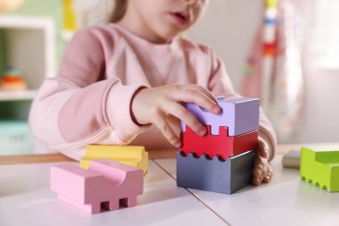 Oyun odasındaki beyaz masada oyuncaklarla oynayan mutlu küçük kız, yakın plan.