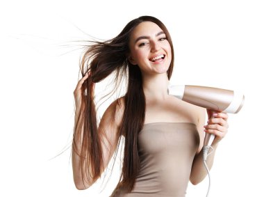 Gülümseyen kadın saçını kurutma makinesiyle beyaz arka planda kurutuyor.