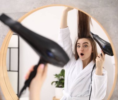 Banyodaki aynanın yanında saçını kurutan bornozlu kadın.