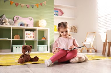 Oyun odasında yerde kitap okuyan küçük bir kız.