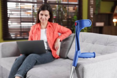 Evdeki koltukta dizüstü bilgisayar kullanan kadın, dirsek değneğine odaklan.