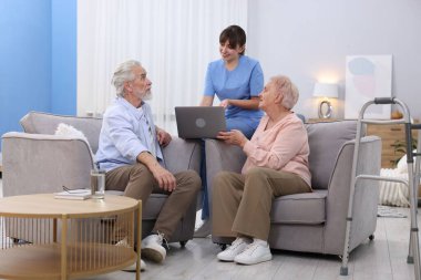 Bakım işçisi üst düzey erkek ve kadınlara huzurevinde dizüstü bilgisayar kullanmayı öğretiyor.