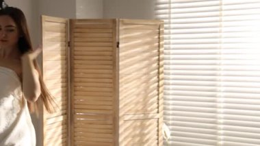 Saçını banyoda saç kurutma makinesiyle kurutan güzel bir kadın. Kamera sola kayıyor.