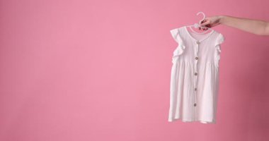 Şık çocuk kıyafetleri ve pembe arka planda ayakkabıları olan kadın, yakın plan.